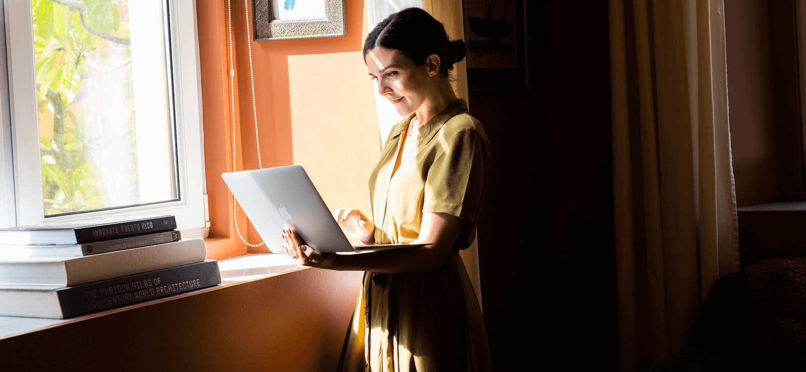 Woman standing at a window holding a laptop and typing