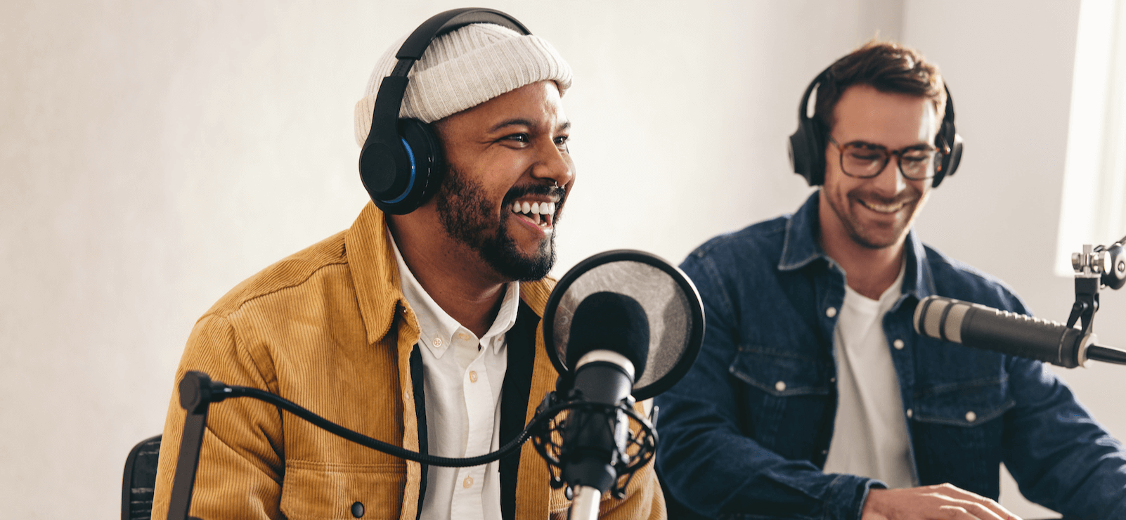 Two people recording a podcast, smiling while speaking into microphones.