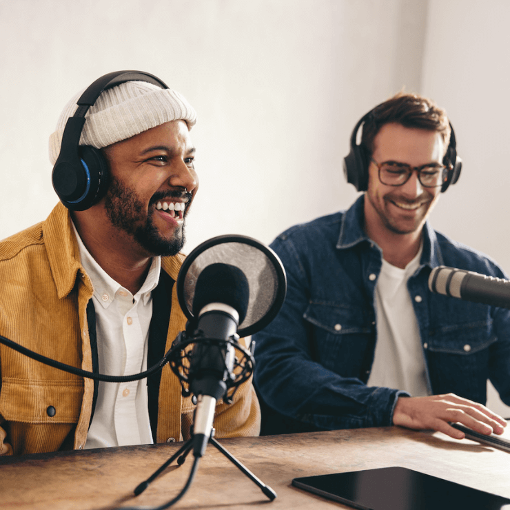 Two people recording a podcast, smiling while speaking into microphones.