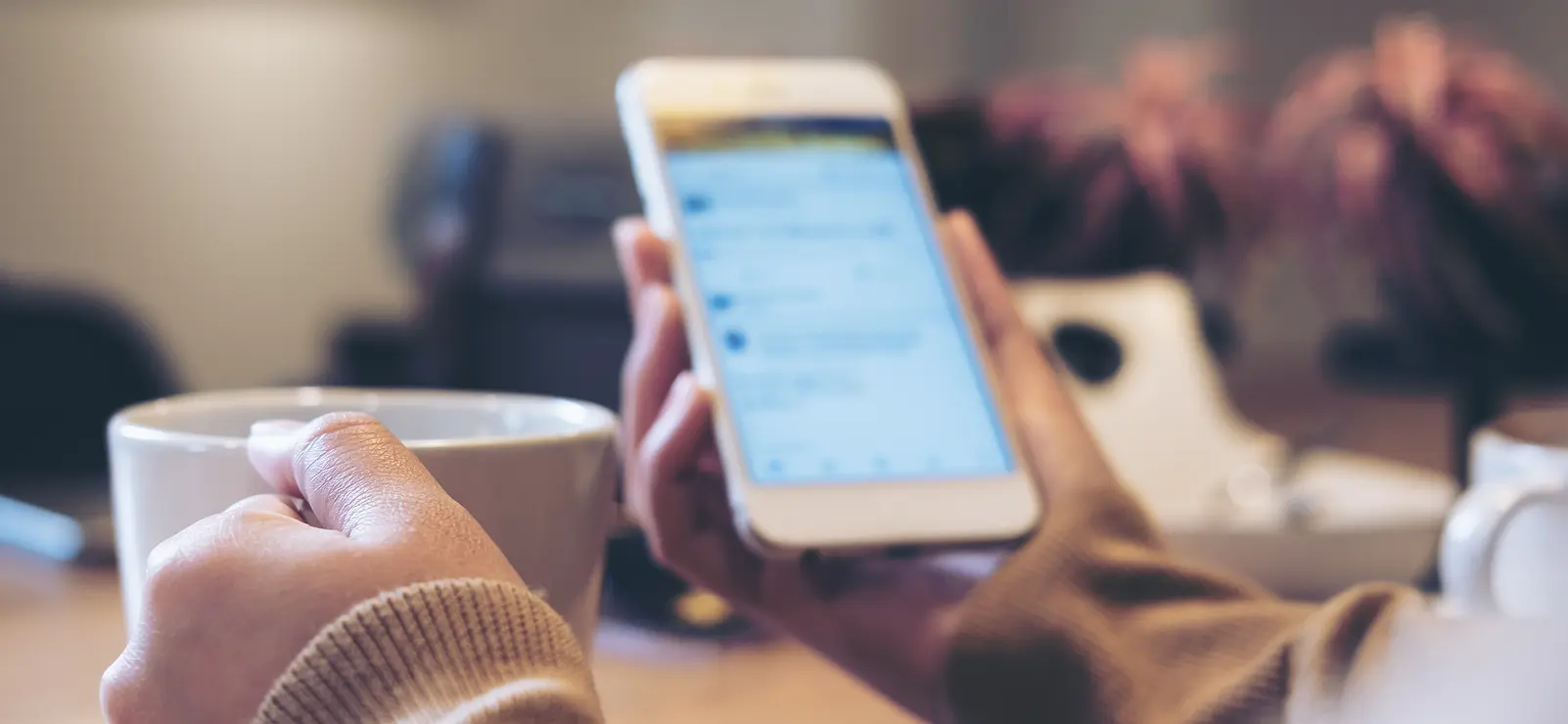 Person looking at a phone while holding a cup of coffee.