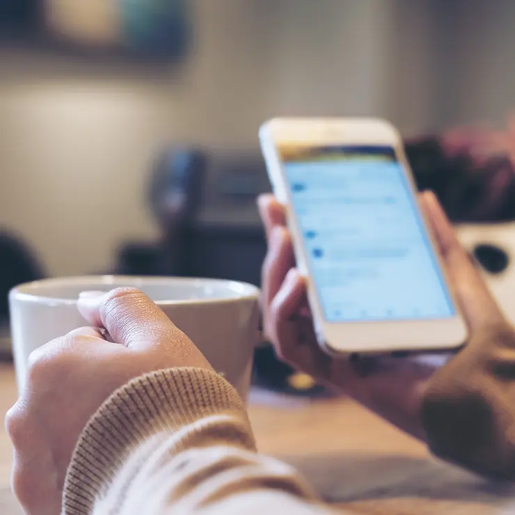 Person looking at a phone while holding a cup of coffee.