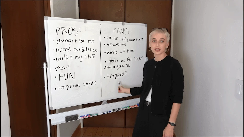 Screenshot of a YouTube video depicting Emma Chamberlain standing in front of a whiteboard depicting pros and cons of an experiment in looking one’s best.